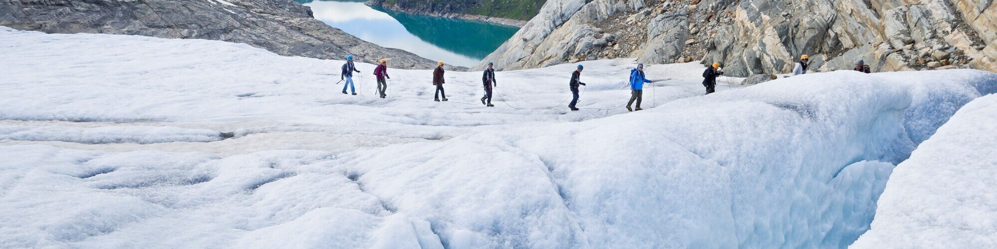 A group of seven people walking on a glacier with lake in the background.