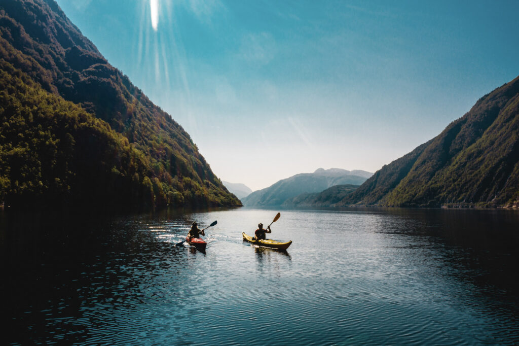 Zwei Personen in einzelnen Kajaks auf einem Fjord an einem sonnigen Tag.