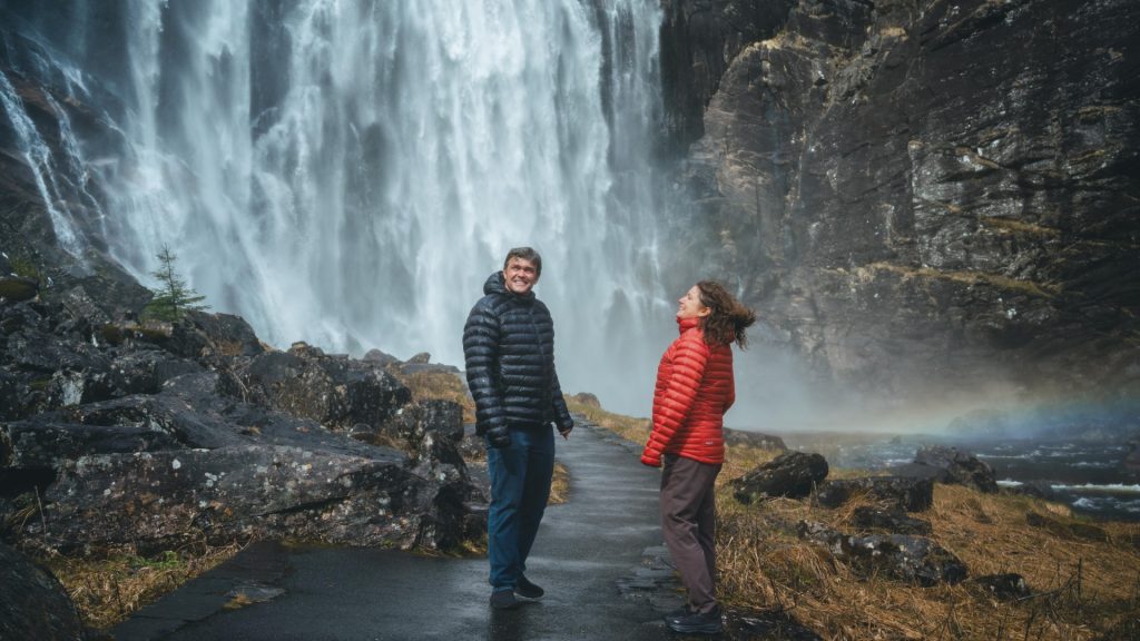 Two persons in front of a waterfall, showered by the waterfall.