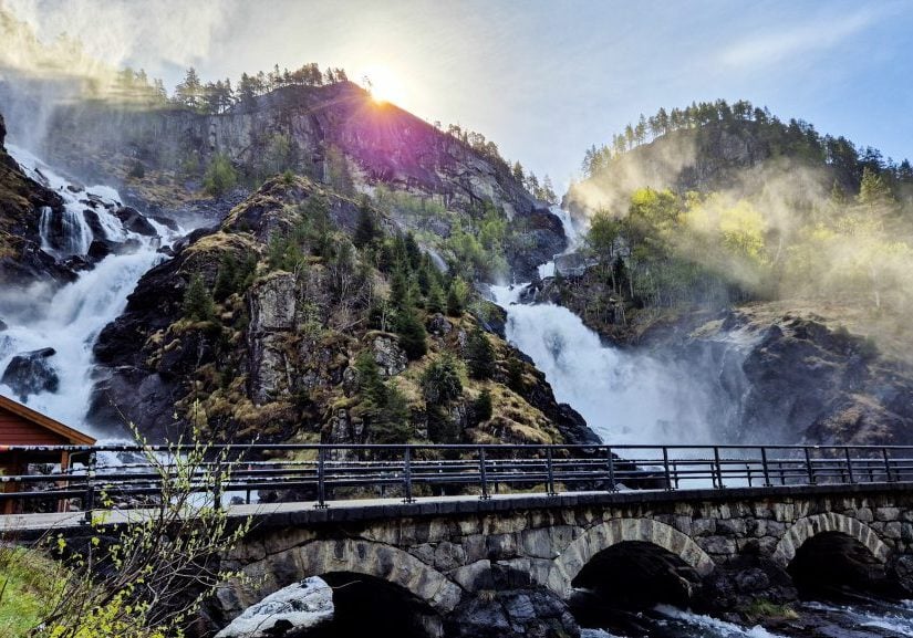 Photo of Låtefoss waterfall near Odda in spring. Sun rising behind at the old bridge in front. 