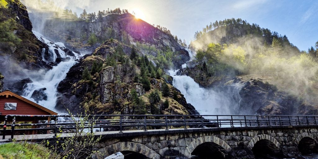 Photo of Låtefoss waterfall near Odda in spring. Sun rising behind at the old bridge in front.