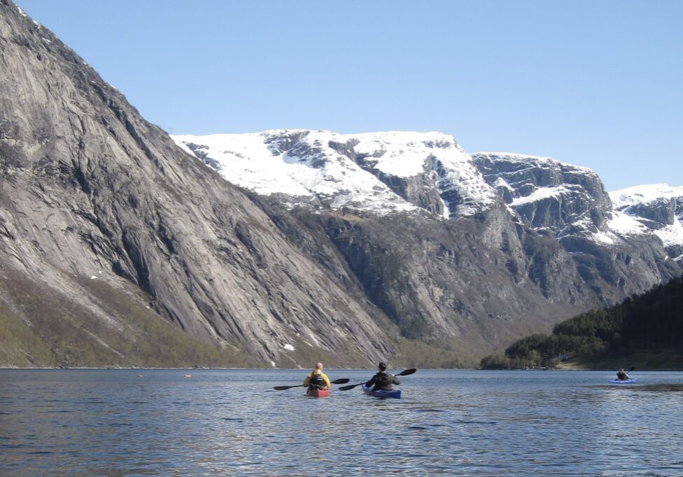 Two people in kayaks on a fjord with snow-covered mountains in the background.