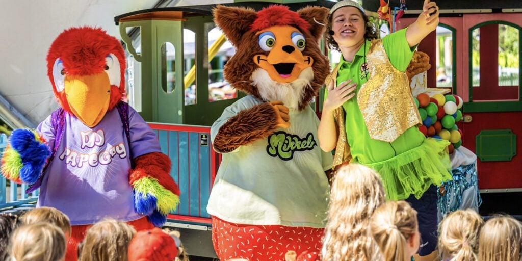Kids watching performance of two stuffed animal figures (people in costumes) and one person showing thumbs up.