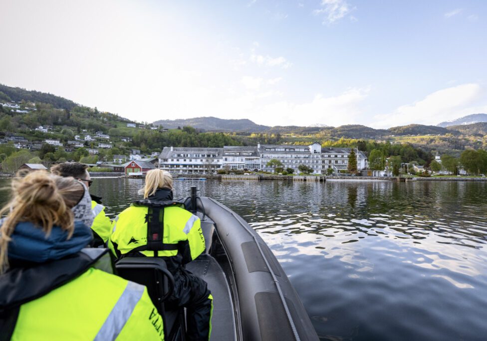 RIB boat with three people in floatation suits approaching shore with a large white hotel.
