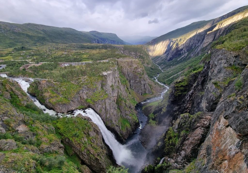A waterfall and a river flowing through a valley on a cloudy day.
