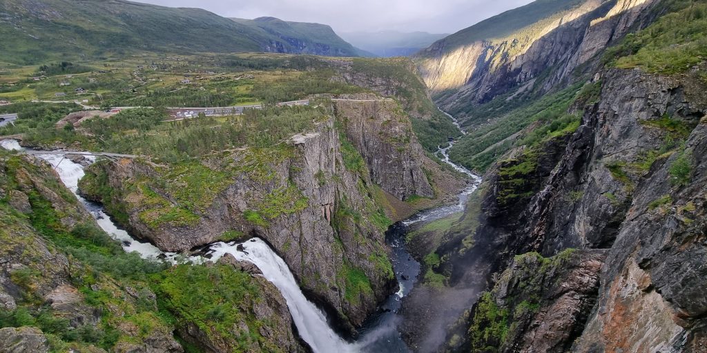 A waterfall and a river flowing through a valley on a cloudy day.